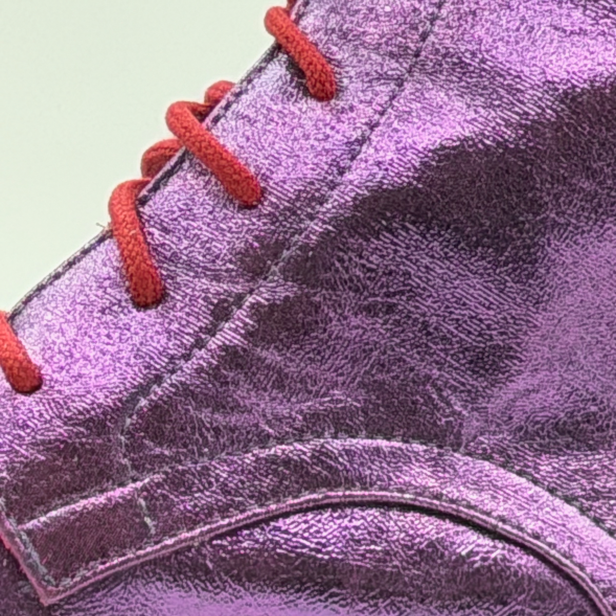Close-up of the Mono Jacarandá tango boot showing the red cotton laces against the crinkled texture of the violet metallic leather