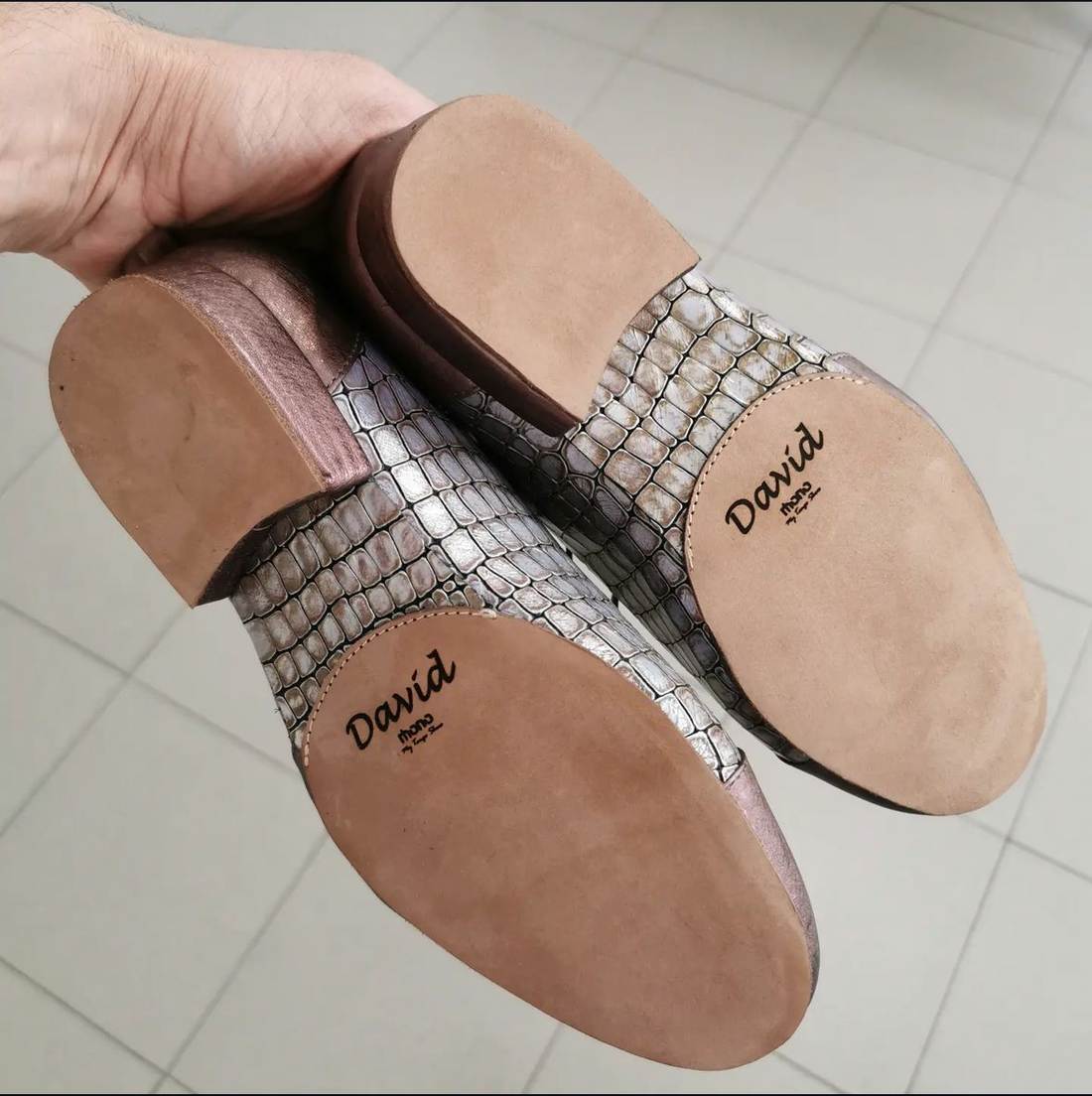 Underside view of a pair of Mono tango shoes in metallic snake-print leather, held up to show the medium leather sole personalized with the wearer's name