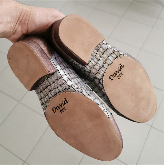 Underside view of a pair of Mono tango shoes in metallic snake-print leather, held up to show the medium leather sole personalized with the wearer's name