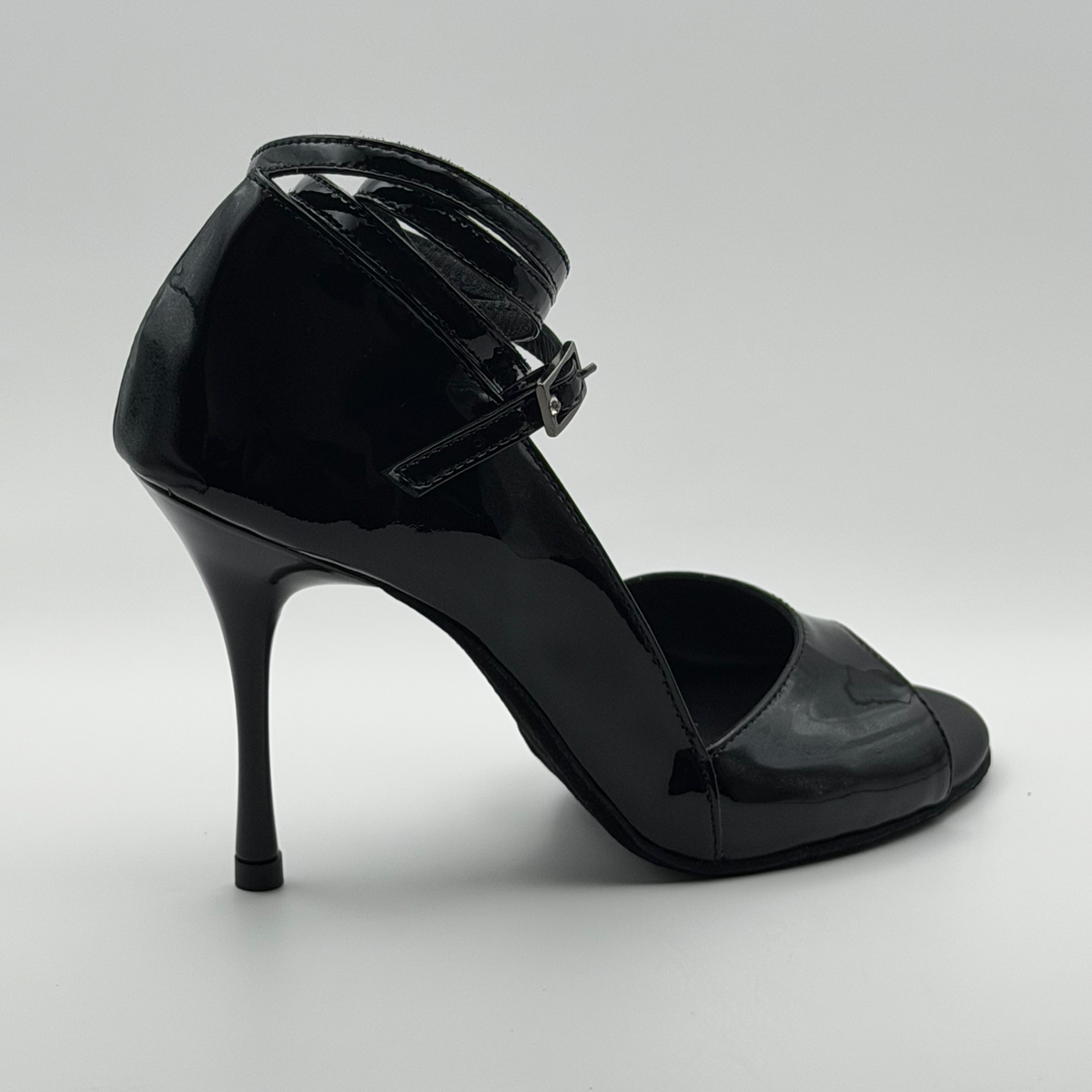 Rear three-quarter view of the Akvile Noir black patent tango heel showing the gunmetal buckle and stiletto heel