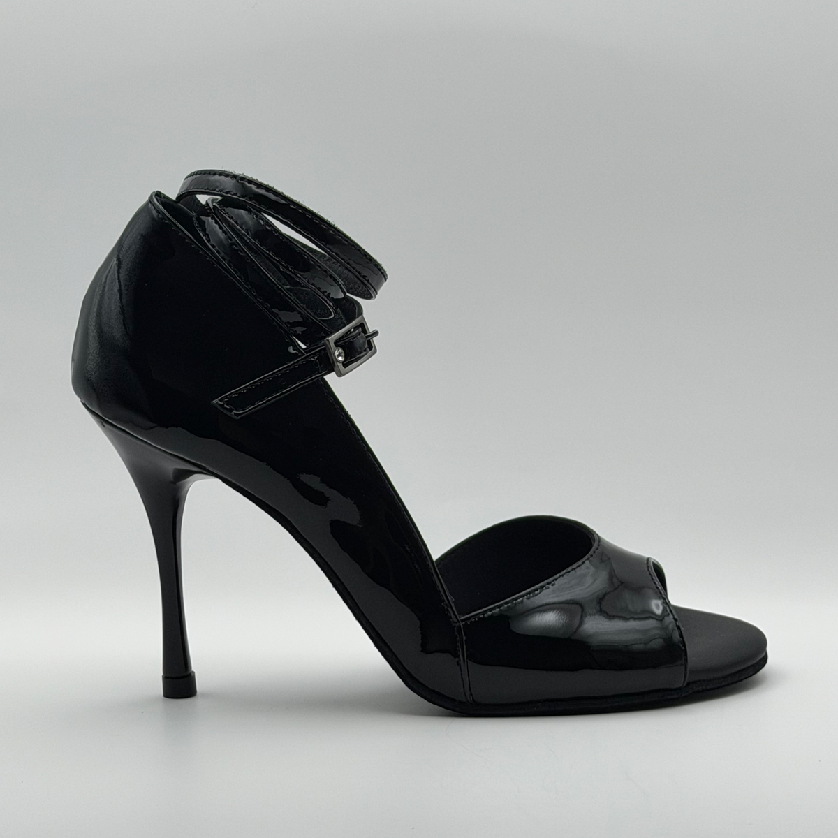 Side profile of the Mono Akvile Noir women's tango heel in glossy black patent leather, showing the wrap ankle strap, open sides, and slender stiletto heel