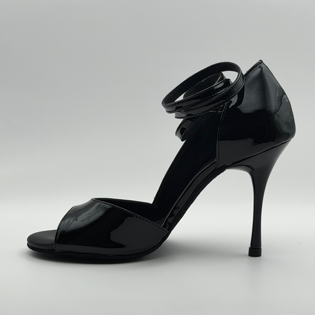 Three-quarter front view of the Akvile Noir tango heel showing the open toe, black footbed, and multi-wrap patent ankle strap