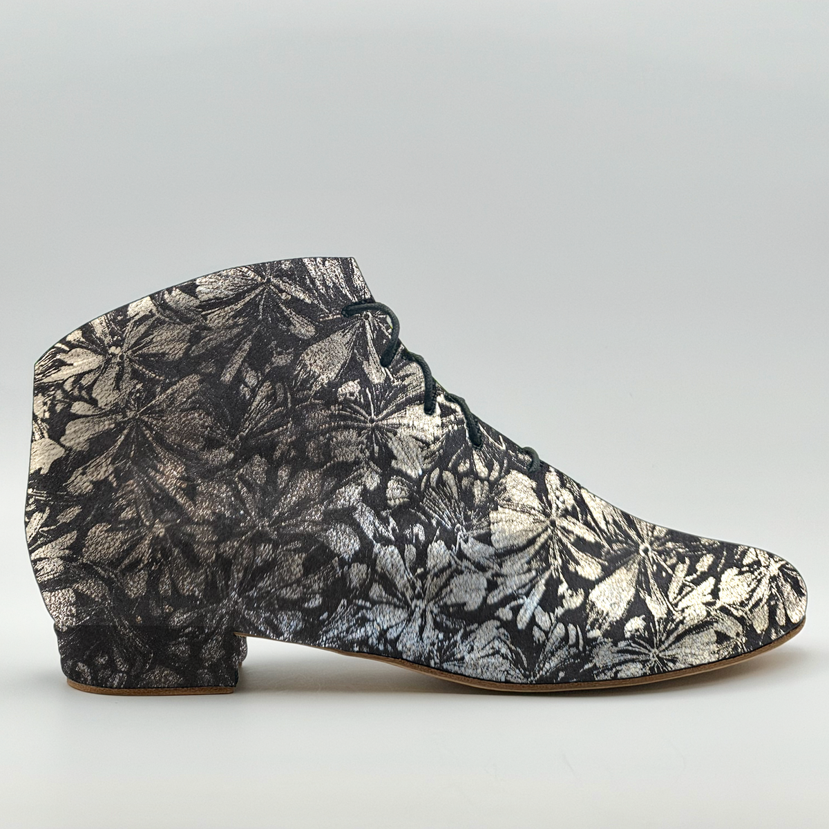Side profile of the Mono Autumn Rising Bottine women's tango bootie in black leather with a silver floral print, showing the charcoal front lacing, almond toe, and low Cuban heel wrapped in the same floral leather