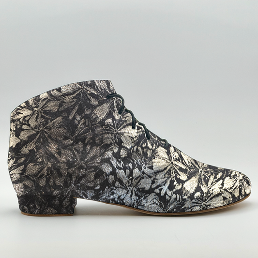 Side profile of the Mono Autumn Rising Bottine women's tango bootie in black leather with a silver floral print, showing the charcoal front lacing, almond toe, and low Cuban heel wrapped in the same floral leather