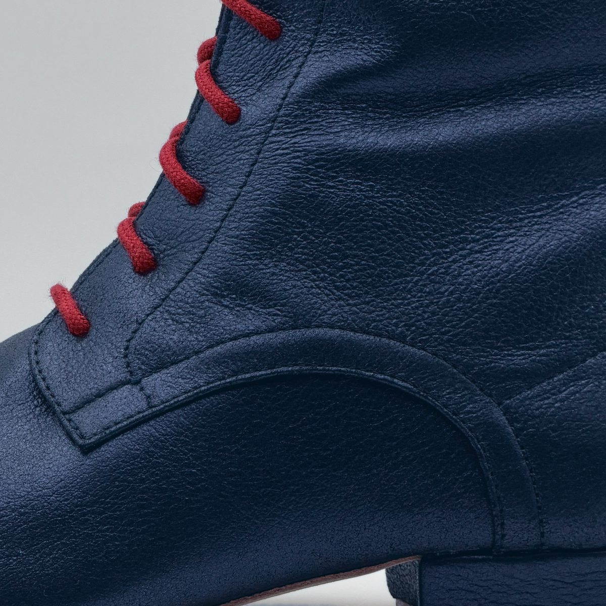 Close-up of the Bleu Marine tango boot showing the red cotton laces and the curved stitched overlay on the textured navy leather
