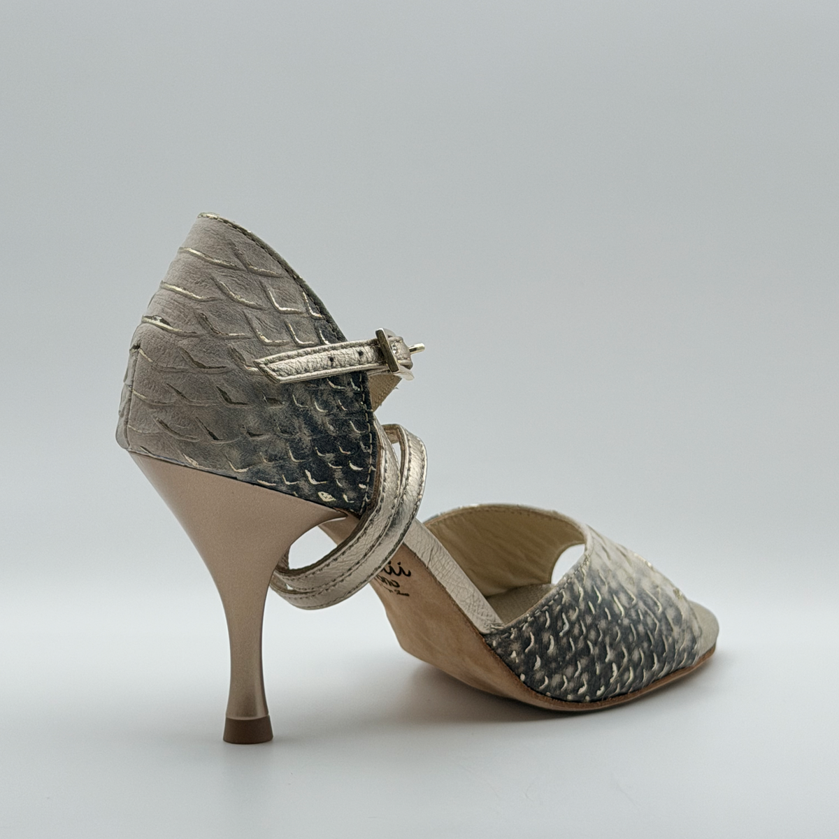 Rear three-quarter view of the Mono Ceniza Dorada tango heel with the gold-tone buckle in focus, showing the adjustable fastening on the signature long strap