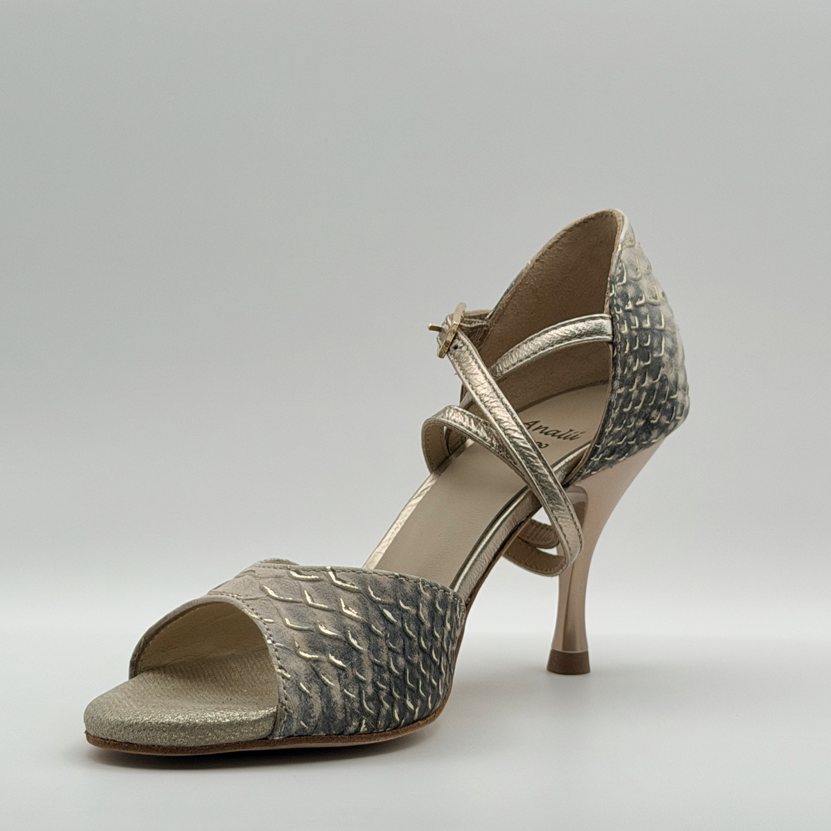 Three-quarter front view from the inner side of the Mono Ceniza Dorada tango heel, showing the cream leather lining and the wrap of the signature long strap
