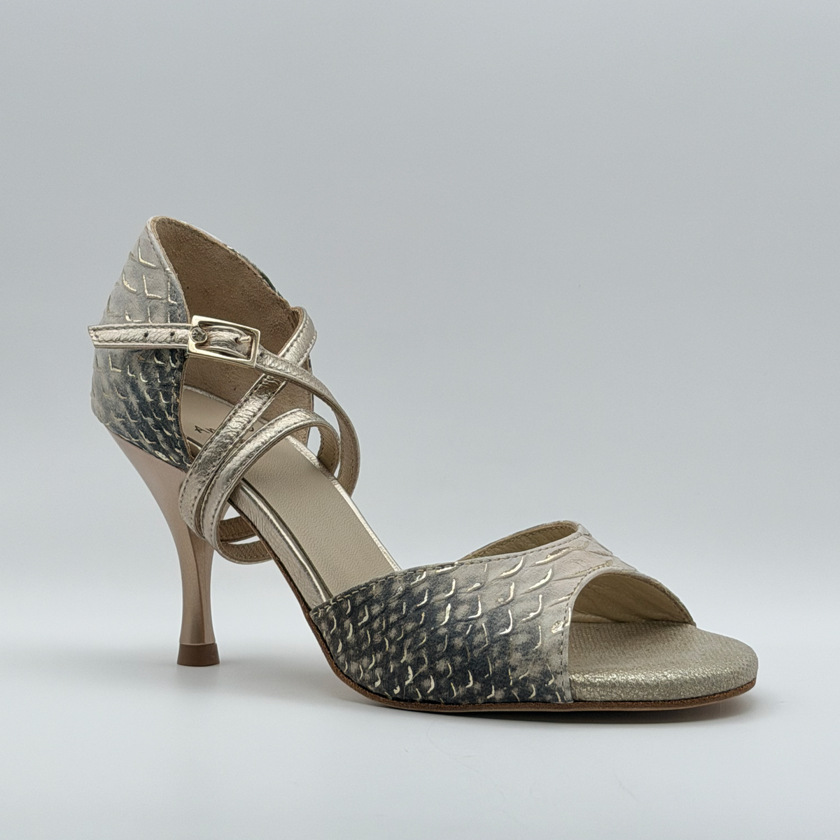 Three-quarter front view of the Mono Ceniza Dorada tango heel showing the open toe over a gold metallic footbed and the gold-tone buckle on the ankle strap