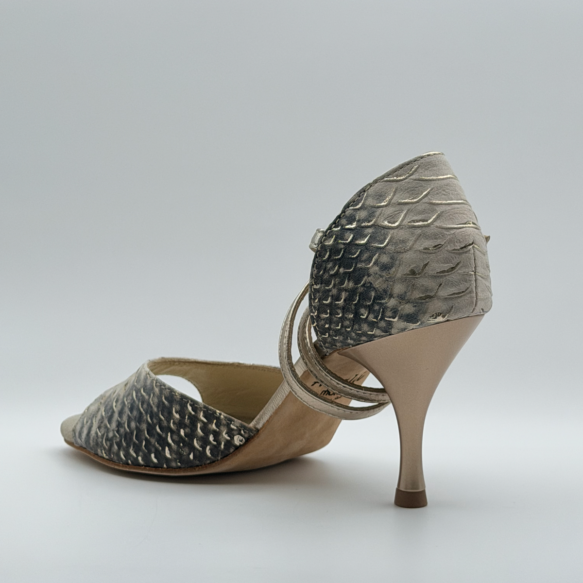 Rear three-quarter view of the Mono Ceniza Dorada tango heel showing the snake-embossed heel cage and the gold strap wrapping behind the ankle