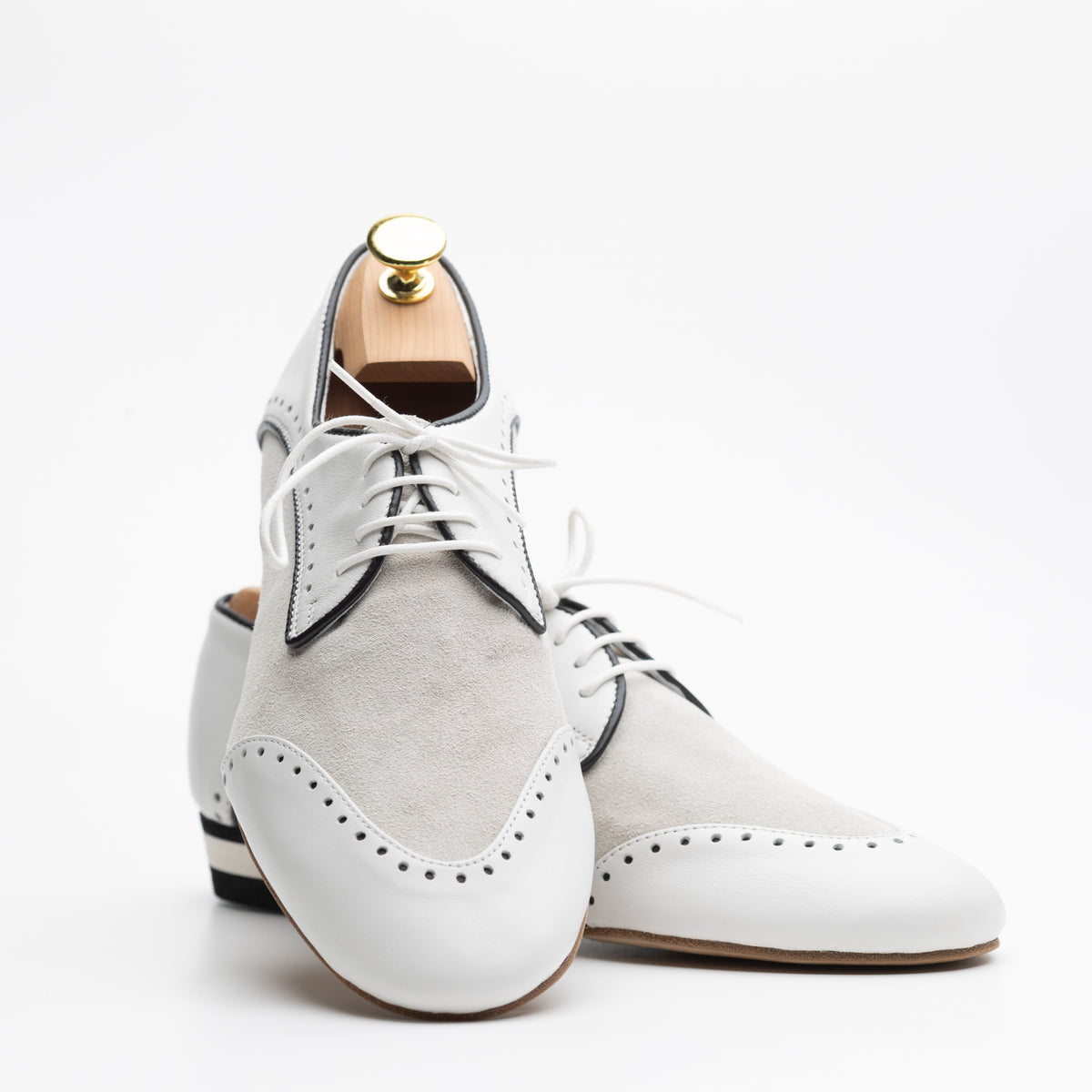 Pair view of Mono El Dandy men's tango Derby, one upright and one laid flat, showing the two-tone white leather and cream suede upper, brogue wingtip perforations, black leather piping, white laces, black and white striped low heel, and natural tan suede outsole.