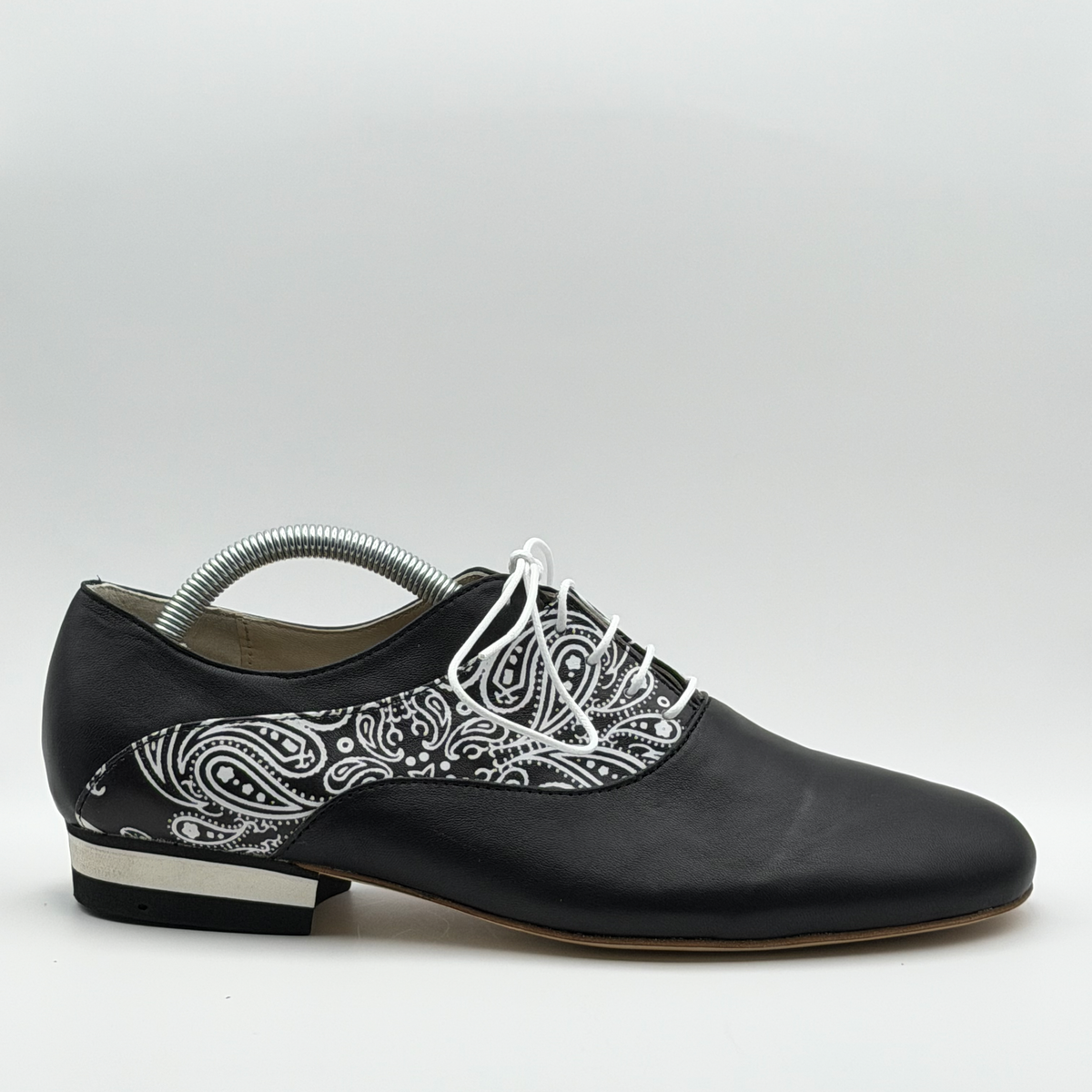 Side profile of the Mono El Pañuelo men's tango oxford in black leather, showing the black-and-white paisley panel sweeping from the laces to the heel