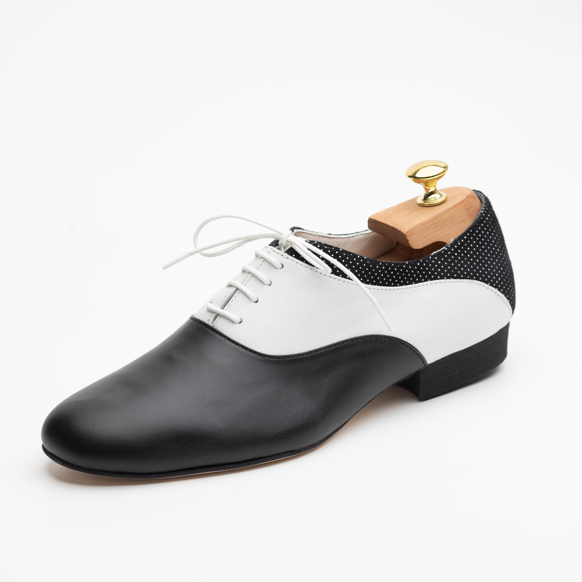 Three-quarter front view of the Mono El Smoking tango oxford showing the closed lacing with white laces and the curved seam between black and white leather