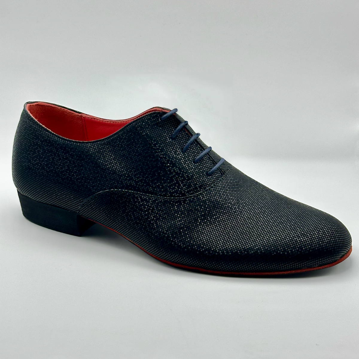 Three-quarter front view of the Mono Fumo di Londra men's tango oxford, showing the black micro-dot finish, closed lacing, red leather lining, and red sole edge