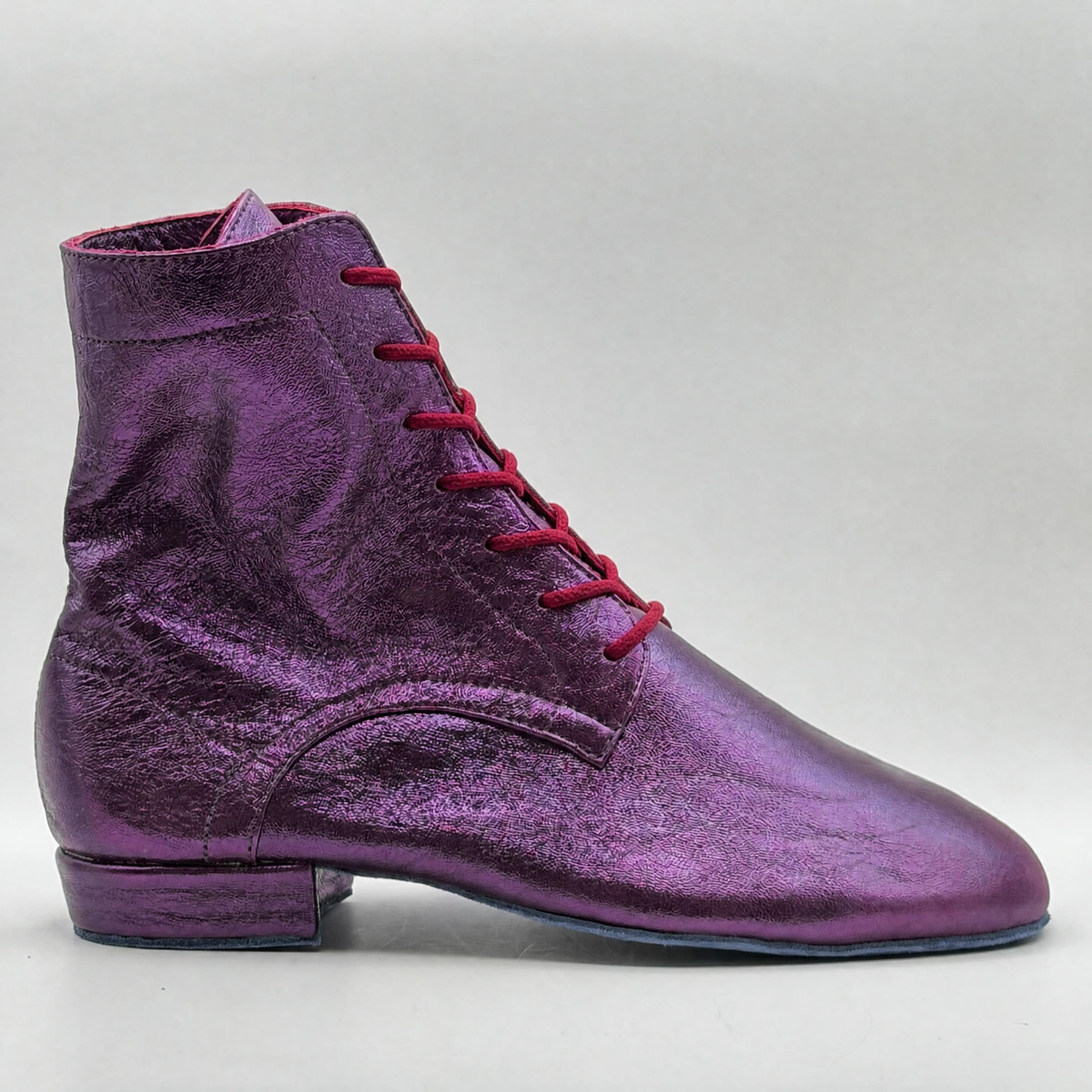 Side profile of the Mono Jacarandá tango boot in violet metallic leather, showing the red laces up the front, the curved heel overlay, and the low Cuban heel