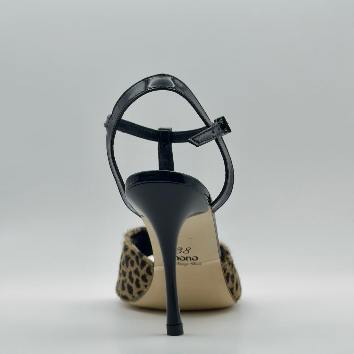 Rear profile of Mono La Fiera women's tango sandal highlighting the open back construction, the black leather lining edge, patent ankle strap, and the elongated stiletto heel from directly behind.