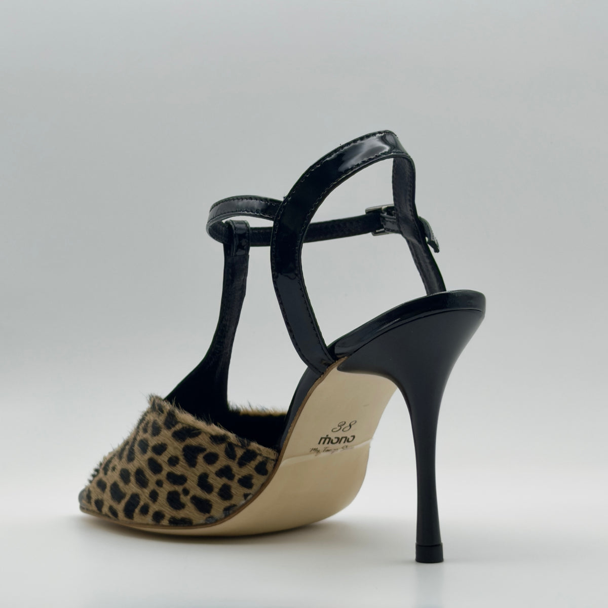 Rear three-quarter view of Mono La Fiera tango sandal showing the back of the T-bar, the patent leather ankle strap loop, black leather heel counter, and slim stiletto from behind.