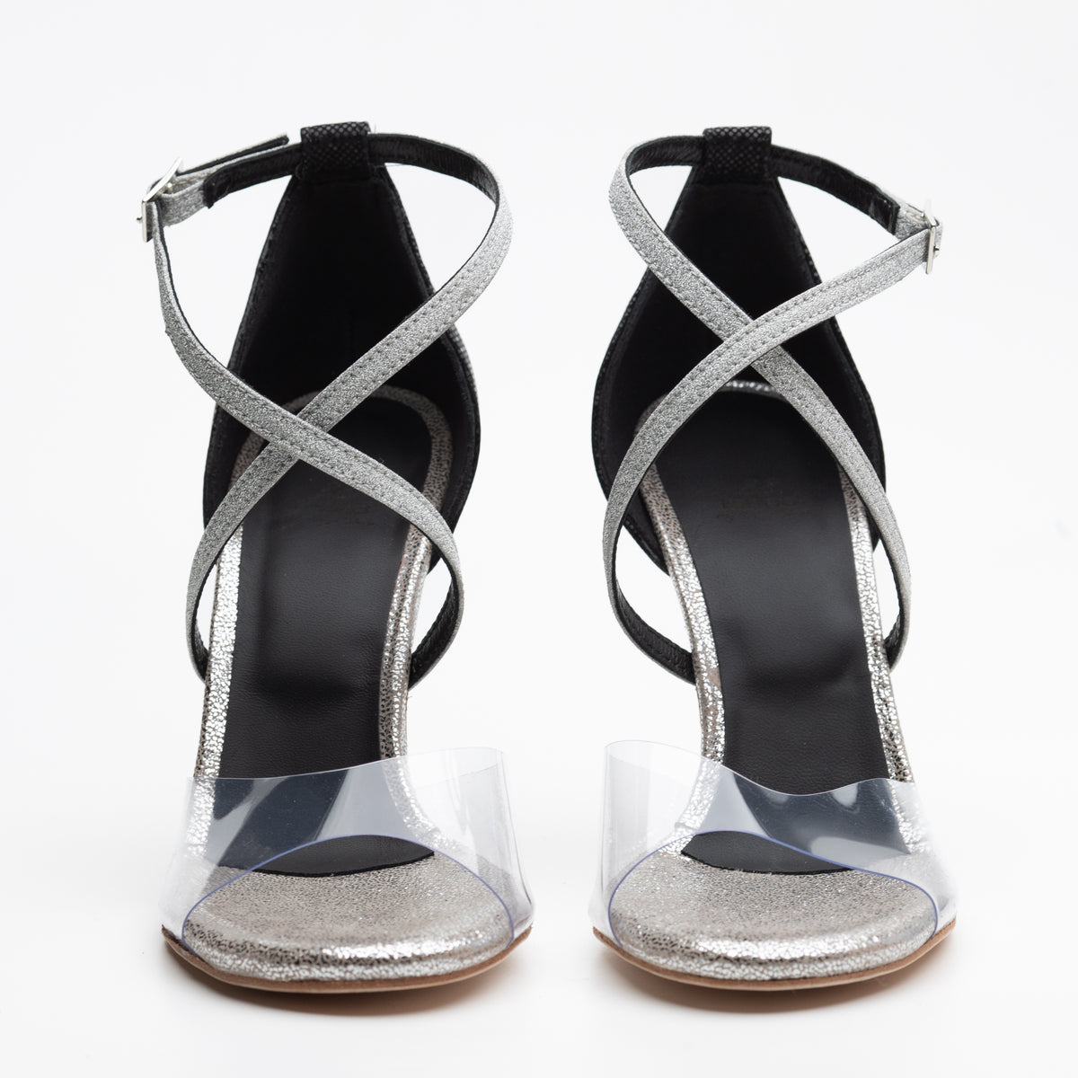 Front-facing pair view of Mono La Plata women's closed-heel tango shoes showing both open toes with silver glitter toe beds under clear PVC vamps, silver glitter crisscross ankle straps, and black fine-grid textured closed heel counters.