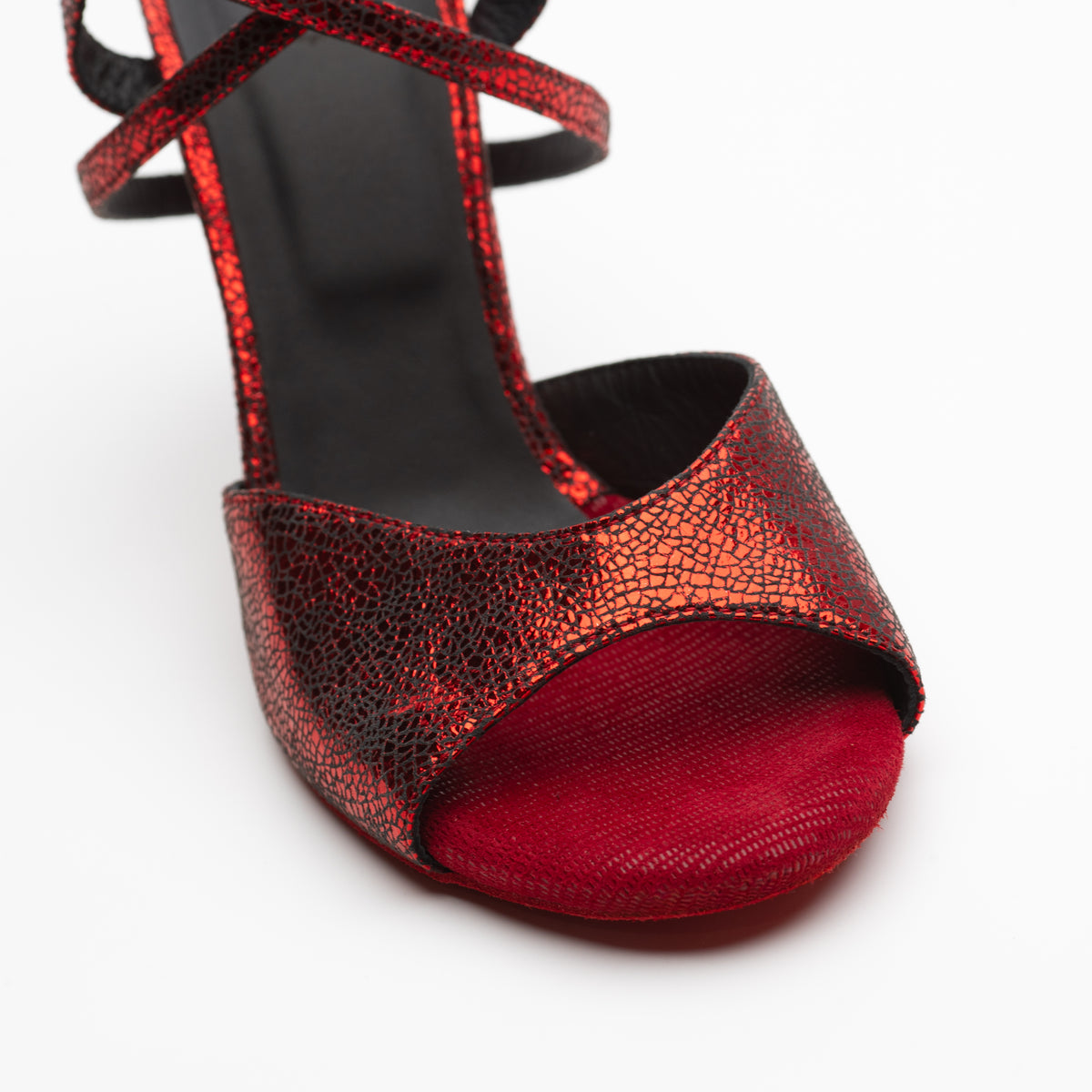 Close-up detail of Mono La Rojita tango sandal vamp showing the open toe, red suede toe bed texture, and red metallic crackle leather upper with cross ankle straps visible above.