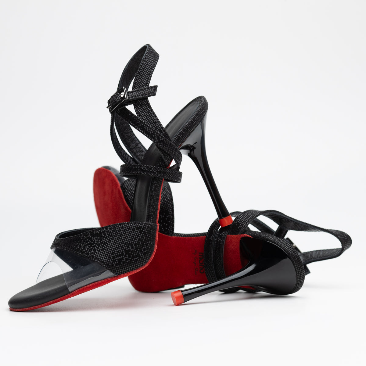 Pair underside view of Mono La Sombra women's tango sandals showing the signature red soles, crossed ankle straps, and slender stiletto heels.