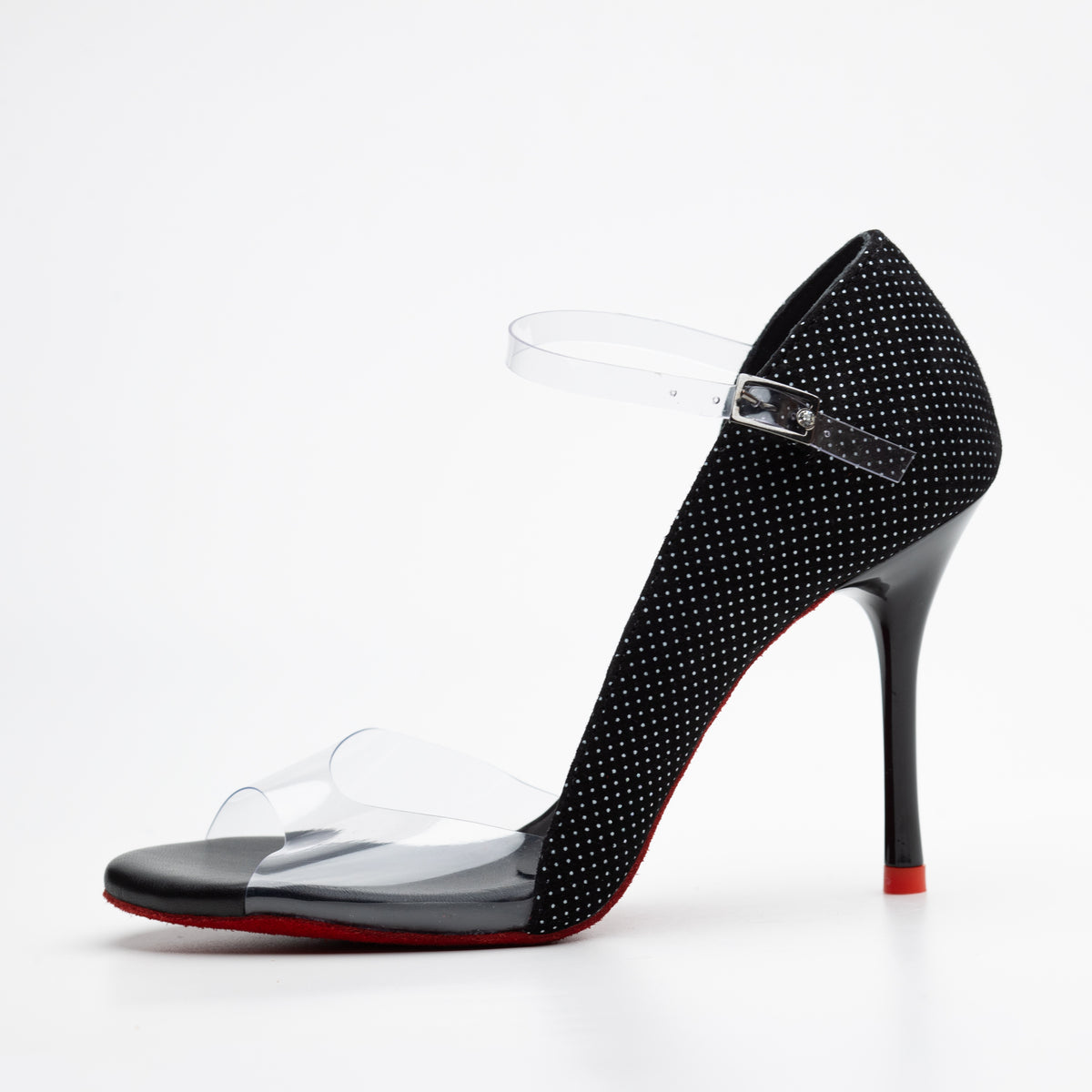 Left side profile of Mono Medianoche women's open-toe tango pump showing the black micro-dot glitter fabric heel counter, clear PVC vamp and ankle strap with silver buckle, slender black stiletto heel, and signature red sole.