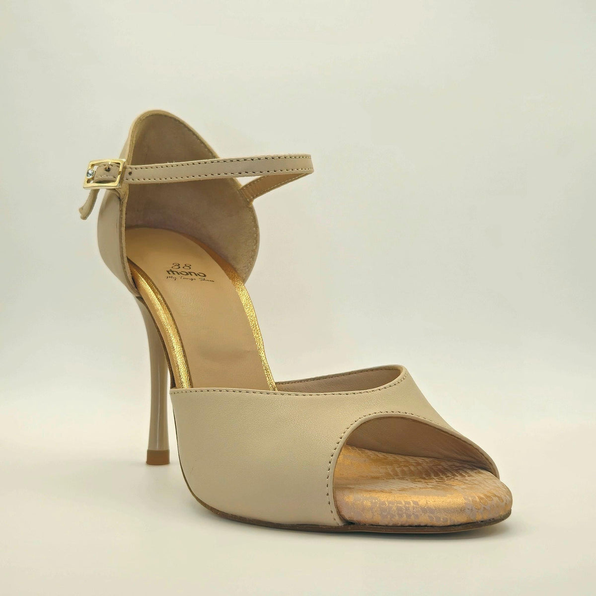 Three-quarter front view of Mono Timeless Nude tango shoe from a slightly higher angle, highlighting the wide peep-toe vamp, gold metallic footbed with Mono My Tango Shoes size stamp, ankle strap with silver buckle at the side, and the full height of the nude stiletto heel.